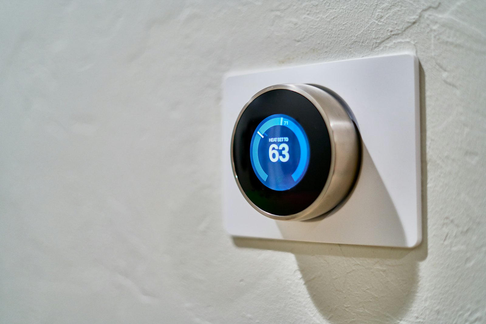 Smart thermostat mounted on a wall showing a 63-degree heating setpoint